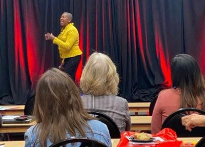 Michelle Perdue speaking on stage with red curtains behind her to an audience