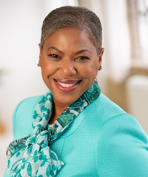 Professional headshot of Michelle Perdue smiling, wearing a teal jacket and scarf