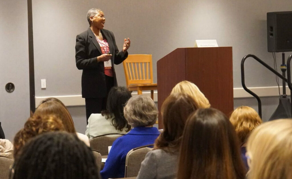Michelle Perdue speaking and gesturing to an audience at a workshop or event