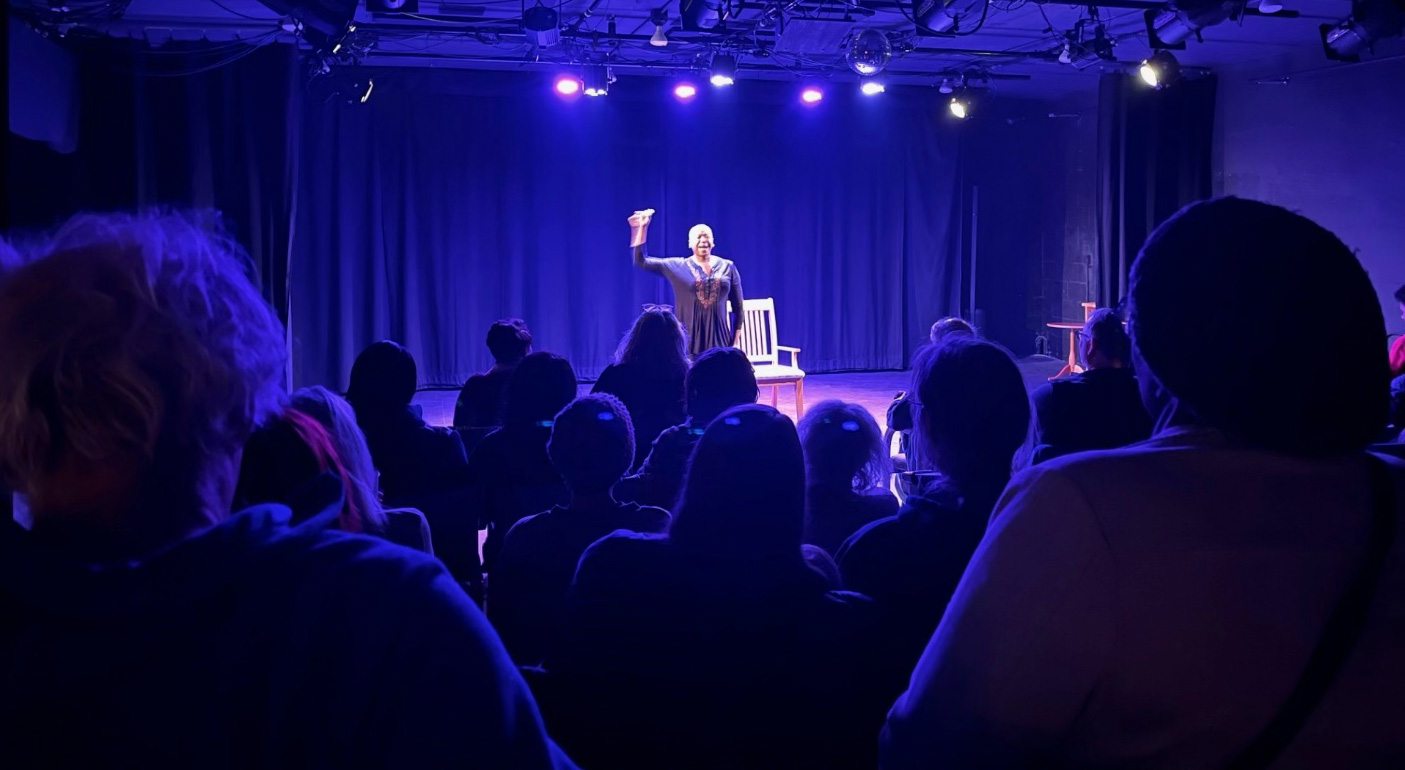 Michelle Perdue speaking on stage under blue lights, viewed from the audience