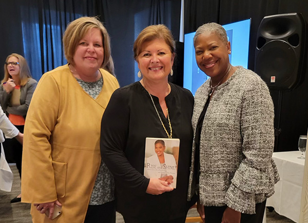 Michelle Perdue with two women, one holding her Rise and Shine book, at an event
